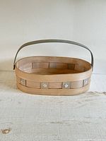 Front view of the oval wood strap basket showing woven construction and flower metal embellishments.