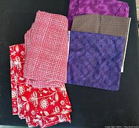Five folded pieces of fabric displayed on a black surface, showing varied patterns and colors including red, purple, and brown.