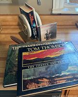 Image showing the two coffee table books 'Tom Thomson: The Silence and the Storm' and 'The Tangled Garden' by J E H MacDonald resting on a wooden surface.