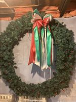 Full view of large circular green wreath with attached multi-colored ribbon bow hanging against a wall.