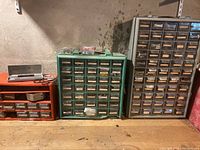 Three organizing cabinets arranged side by side against a basement wall, various small hardware items in drawers