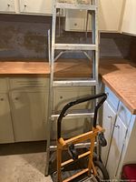 Metal step ladder standing upright in basement beside wooden counter and white cabinets