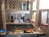 Full shelf with funnels, flashlights, wheelbarrow inner tube, caulking tool, crowbar, chisels, and other hand tools.