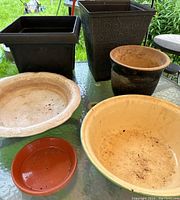 Full view of all six pots including the two large black plastic pots, the antique white enamel basin, the smaller black clay pot, the red clay saucer, and the beige shallow clay dish.