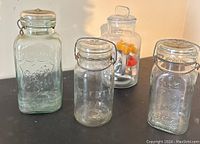Four jars on black tabletop, one with colorful plastic cookie cutters inside, three with embossed seals: Perfect Seal, Safety Seal, Queen Seal.