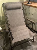 Front view of one beige folding lawn chair with metal frame, reclining feature, fabric seating and cushioned rolled headrest