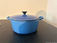 Side view of blue round cast iron Dutch oven with lid, showing handles and exterior color.