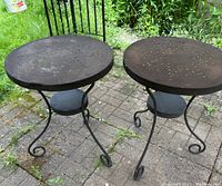 Two dark brown metal patio tables with round perforated tops and decorative scroll metal legs. One table has a small dent on the edge.