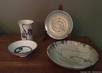All four pottery pieces displayed together on a table with a plate stand holding the small plate upright in the back.