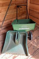 Scotts Standard broadcast spreader and large outdoor dustpan together in shed with dirt and signs of use.