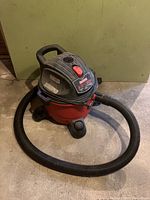 Full view of Craftsman red and black shop vacuum with flexible hose on concrete floor.