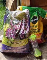 Two bags of soil placed side by side, one Miracle-Gro potting mix and one Veranda container mix. A green insect trap is positioned in front of the bags.
