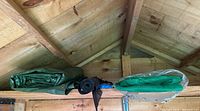 Wide shot of green tarp, black landscape fabric roll, and green shade cloth stored on shed ceiling beams