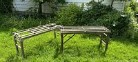 Two wooden tub benches placed on green grass outdoors showing rustic condition and slatted design.