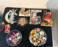 Overview of various vintage Christmas cardboard hangers and two bowls of assorted vintage glass Christmas ornaments.