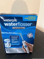 Front and side view of Waterpik Waterflosser Ultra box showing branding, use imagery, and product claims.