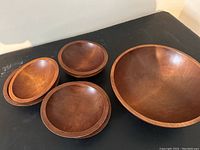Photo showing one large round wooden serving bowl and three smaller individual wooden bowls arranged on a black surface.