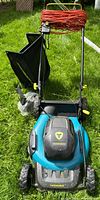 Full view of Yardworks electric lawnmower with orange extension cord wrapped on handlebar, mounted grass catcher bag, and wheels visible.