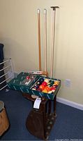 Full lot showing billiard balls box, cues, extender, and cue holder rack in dark wood