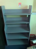Front view of blue enameled 5-tier wood bookcase against a wall, showing all shelves and solid side panels.