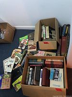 Boxes filled with assorted hardcover and paperback books scattered and stacked in boxes and on the floor