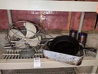 Lodge cast iron fry pan resting in a metal roasting pan with surface rust, next to a vintage Westinghouse metal fan and two empty tea canisters with purple lids.