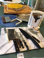 Overview of cutting boards, knives, rotary cheese slicer, metal serving tray, yellow cast iron trivet, and plastic kitchen tool.