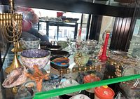 Shelf display showing brass menorah, assorted pottery bowls with colors and chips, geode specimens, and various candle holders