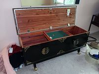 Open top view of black Lane cedar chest showing three internal compartments and green felt lining in center section. Chest has brass corner accents and Asian design motifs on the exterior.