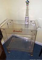 Frangelico branded Lucite bar cart with Galliano liquor bottle on top
