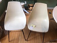 Pair of off-white mid century modern scoop chairs with molded resin seats and metal legs on wood floor.