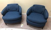 Pair of blue upholstered mid century style armchairs positioned side by side on carpeted floor.