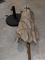 Photo of the patio umbrella folded with beige fabric and brown pole laying on floor next to the heavy metal base.