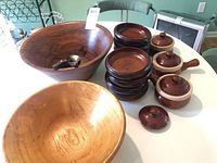 Overview photo showing the large walnut salad bowl, smaller stacked walnut bowls, and six ceramic covered soup crocks with lids and handles displayed on a white surface.
