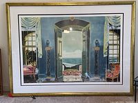 Framed lithograph showing an interior room with blue walls, two curtained windows, two columns, and an open door overlooking the sea coastline.