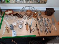 Full lot overview of silver plated cutlery, serving utensils, baskets, glass coasters, and decorative items arranged on a table.