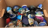Box containing about two dozen assorted souvenir snow globes with various bases, colors and miniature scenes, some missing or partially filled with water.