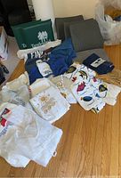 Wide angle showing the assortment of beach towels, cover ups, seat cushions, back support cushions, and sweatshirt spread on the floor.