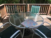 Glass top round table with white metal frame and four white metal frame chairs with green mesh seats and backs, tablecloth folded on table.