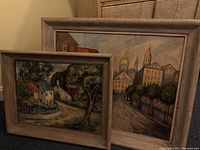 Two framed oil paintings side by side against a wall, showing parts of the two artworks