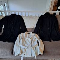 Three women's wool coats displayed on couch: two black coats and one white coat.