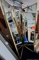Photo of 4 full-length mirror sliding closet doors with gold frames, standing upright in storage area.