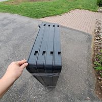 Side view of the four black plastic utility shelves stacked and held by hand, showing the narrow profile and similar design.