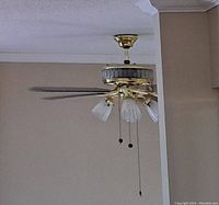 Photo showing 52 inch ceiling fan mounted on ceiling with brass finish, four blades, and four downward-facing glass light shades. Two pull chains visible.