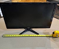 Acer computer monitor with tape measure indicating screen dimensions on countertop surface.