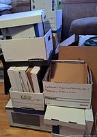 Stack of Bankers Boxes and Staples storage boxes on living room floor, some labeled for content organization.