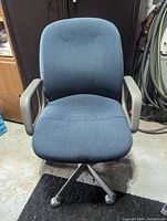 Front view of blue office chair showing fabric seat, padded backrest, grey armrests, and caster wheel base.