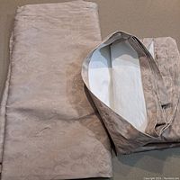 Taupe blackout curtains folded, showing floral jacquard pattern and white lining.