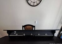 Front view of the black wooden wall shelf with five silver metal hooks mounted below the shelf.