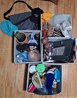 Overview photo of all miscellaneous items including duffel bag, caps, boxes, kitchenware, hangers, and knitted goods.